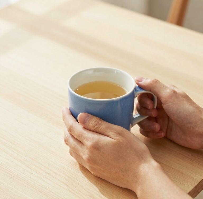 Eye-level 35mm photograph of hands holding a warm ceramic mug on a light wooden table, soft morning sunlight casting gentle shadows.