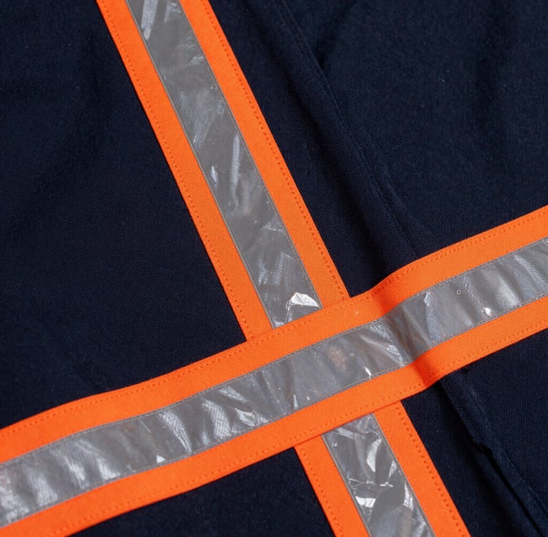 Close-up of high-visibility reflective strips and orange double-stitching on a dark navy PEMEX uniform fabric, industrial workshop lighting