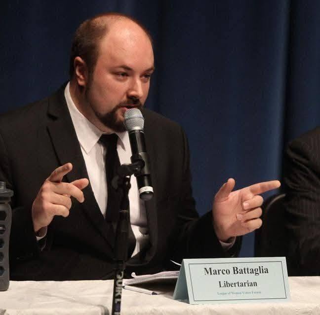 Libertarian candidate Marco Battaglia speaking at a microphone during a political forum event.
