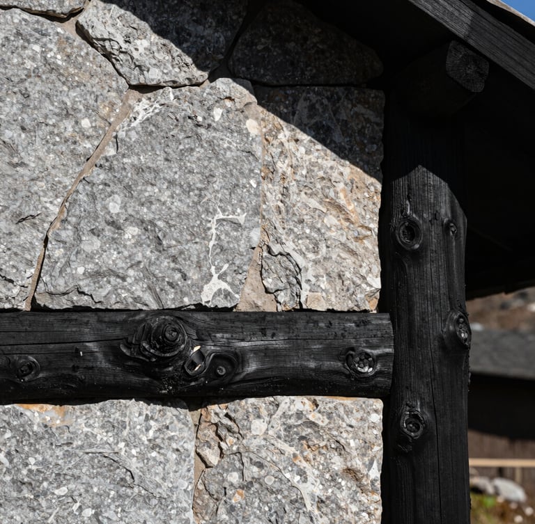A sharp, high-contrast architectural detail of raw honed stone and charred timber under harsh high-altitude mountain sunlight casting deep shadows