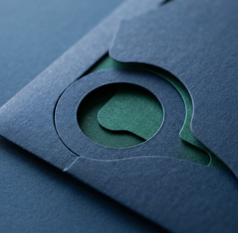 Macro close-up of a high-quality physical direct mail piece with sharp custom die-cuts, textured premium paper, resting on a clean dark blue desk under bright natural daylight.