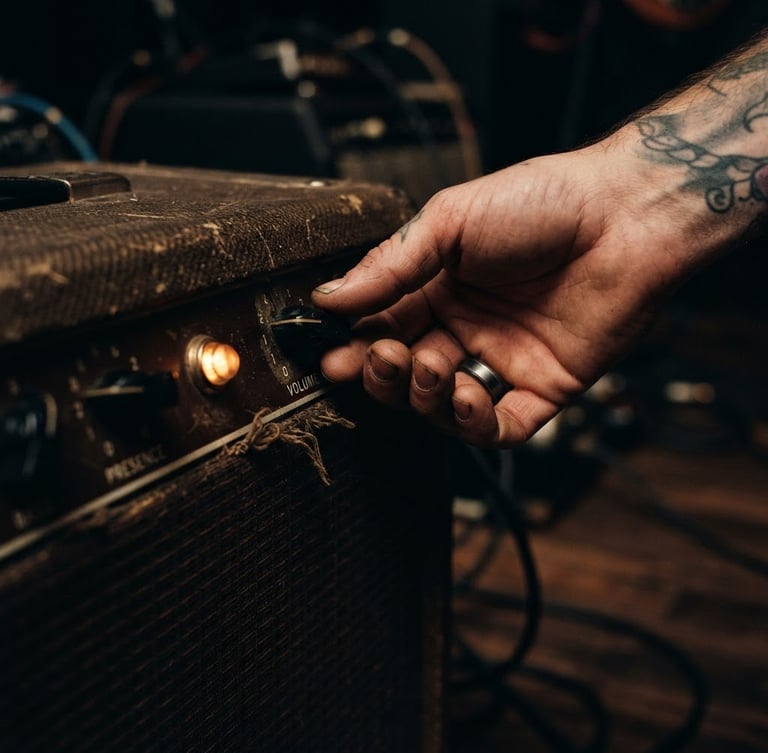 Close-up of weathered hands adjusting the volume knob of a vintage tube amplifier, warm tungsten pilot light glowing amber in a dark room, 35mm film grain