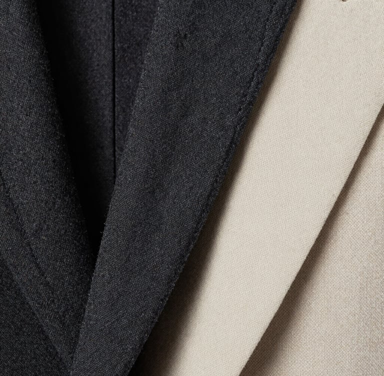 Close-up macro shot of high-quality charcoal wool textile and precise double-stitching on a blazer lapel, high-contrast studio lighting, sharp focus, 35mm lens