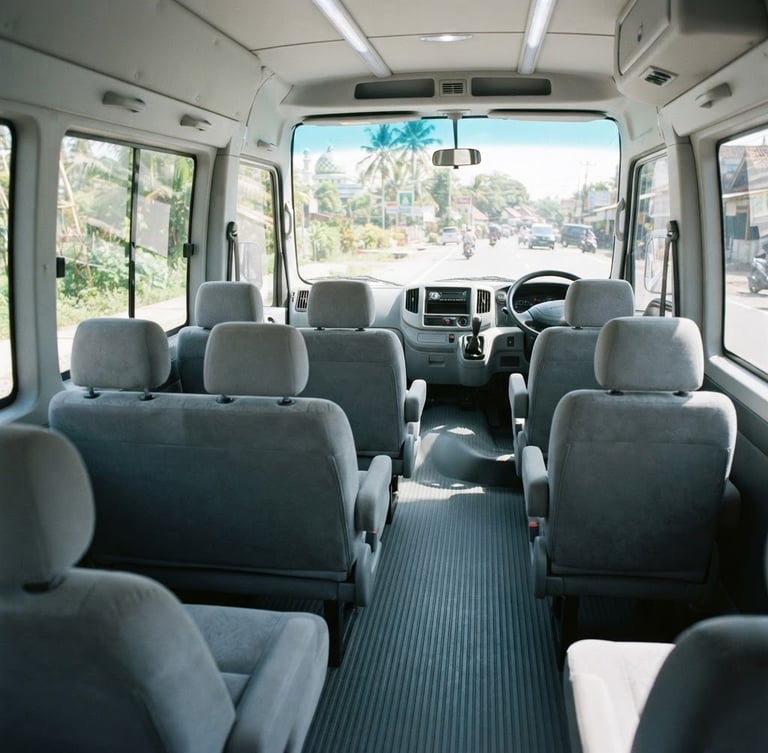 Wide-angle interior shot of a clean, spacious Isuzu ELF microbus cabin, bright Indonesian daylight streaming through windows, plush grey seats, immaculate dashboard, 35mm lens