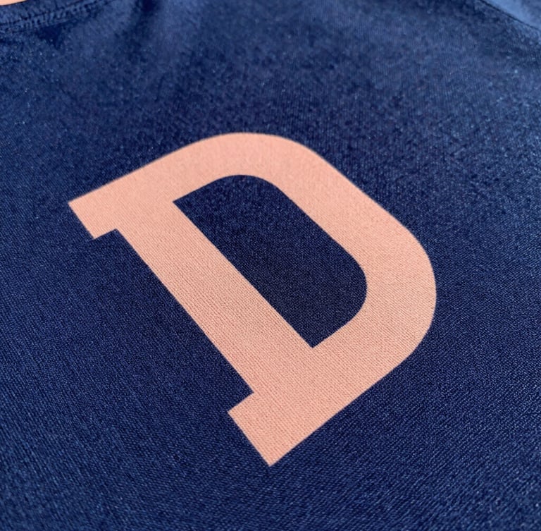 Close-up shot of rich navy fabric texture with a crisp peach-colored DTF print, natural daylight, sharp focus on thread detail, 50mm lens