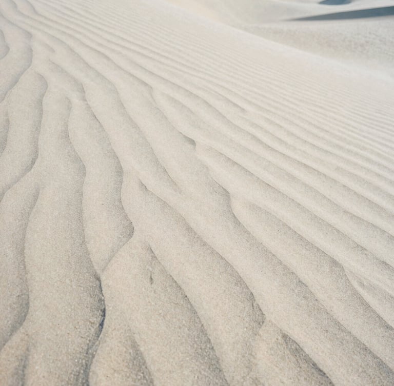 A close-up photograph of wind-swept sand dunes with sharp shadows, soft natural morning light, minimalist composition, medium format film texture.