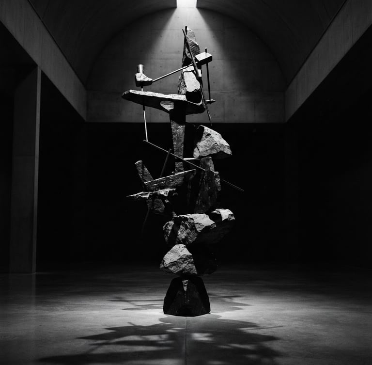 Stark monochrome gallery photography, dramatic chiaroscuro spotlighting, a towering balancing sculpture of bronze and stone in an empty high-ceilinged museum hall, deep obsidian shadows, 35mm