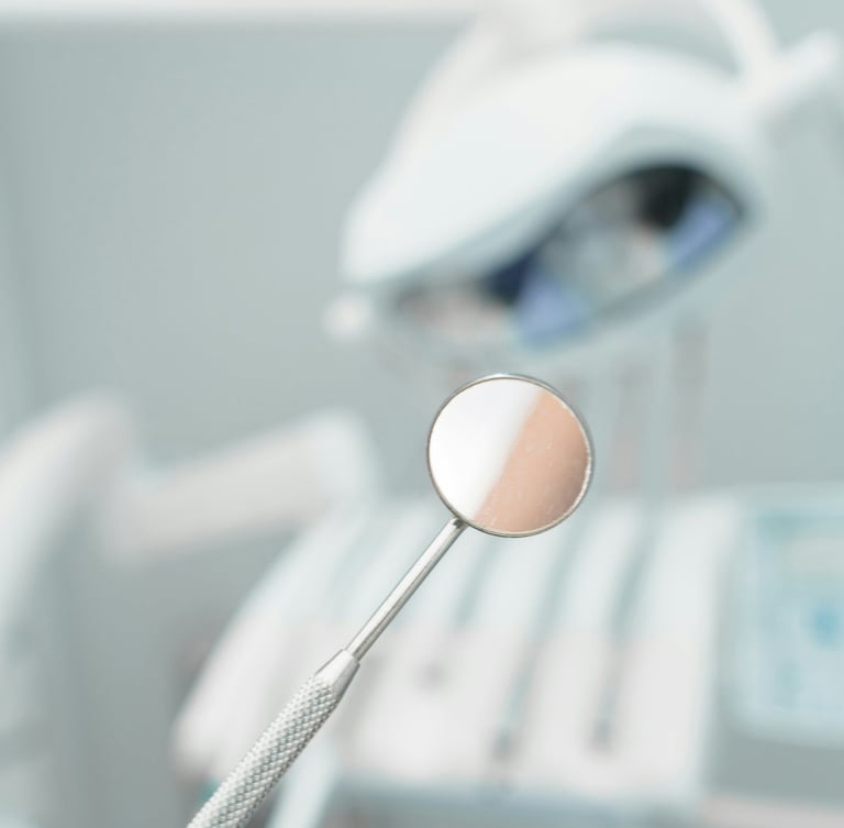 A stainless steel dental mirror held in focus within a modern dental office setting.