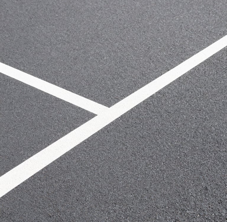 Extreme close-up of textured acrylic court surface grain, sharp geometric white line cutting diagonally, direct bright sunlight showing high-contrast texture.