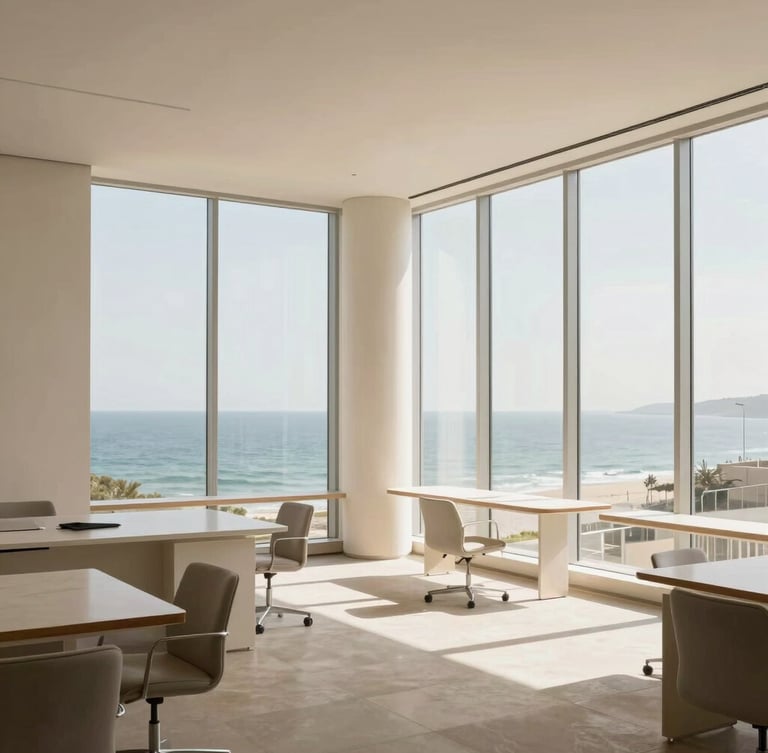 Architectural interior photography of a sunlit, clean modern office space, soft coastal daylight streaming through tall windows, minimal furniture, clean lines, slate and warm cream tones, 35mm