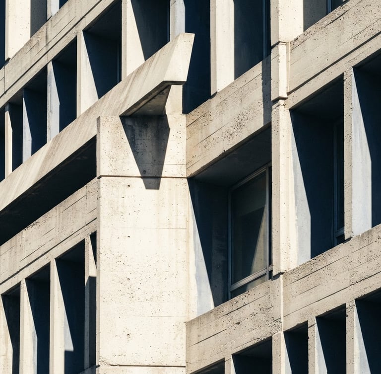 Macro architectural crop of a modern concrete building facade, sharp diagonal shadows, high-contrast daylight, desaturated navy tones, 50mm lens