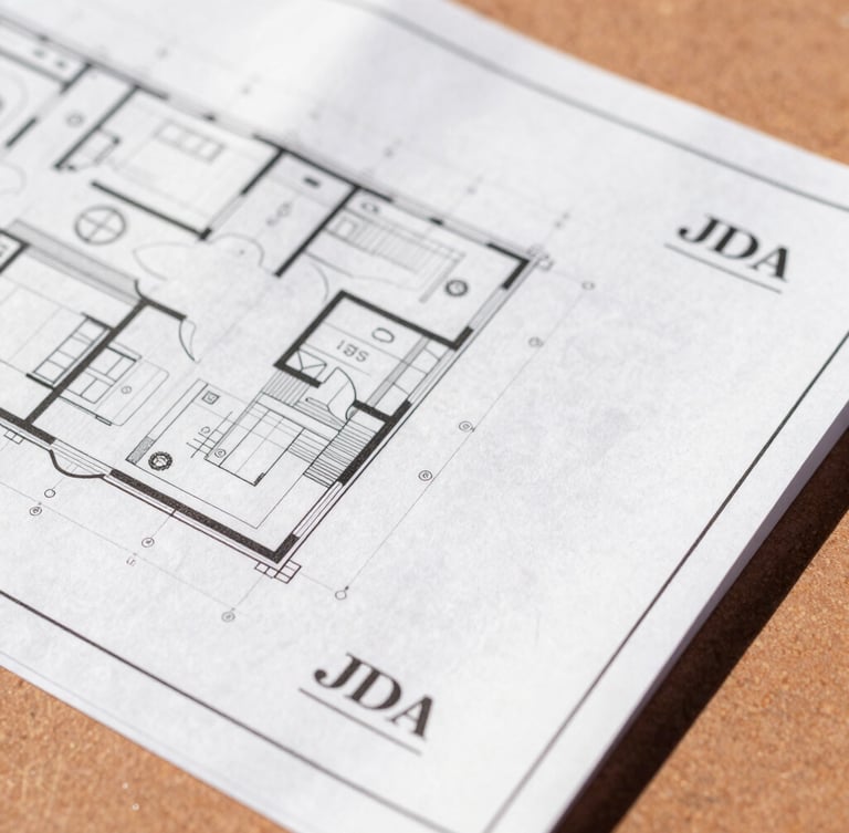 Close-up of clean, organized architectural blueprints and official JDA stamp documents resting on a warm terracotta surface under bright afternoon sunlight, 35mm lens