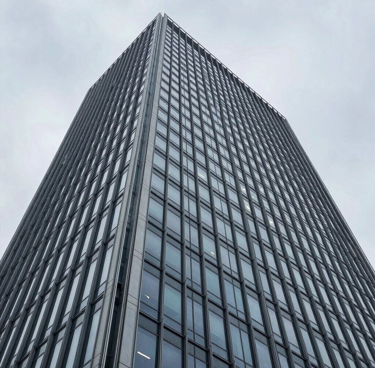 Wide-angle architectural photograph of a modern steel and glass skyscraper facade, sharp overcast daylight, cool desaturated blue and slate tones, high-contrast structural composition