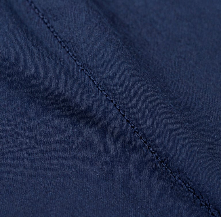Macro extreme close-up of double-stitched seams on a heavy navy cotton garment, soft diffused studio light, crisp detail, 50mm lens