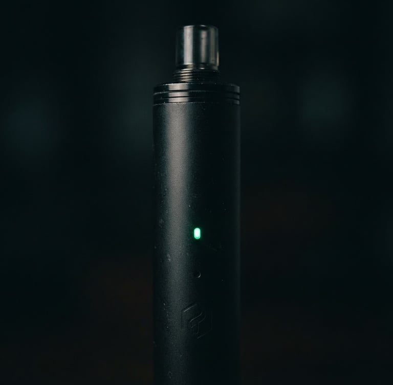 Sleek close-up of a matte black vape device with a subtle emerald green light glowing on its indicator, dark low-key lighting, highly detailed macro shot, 50mm lens