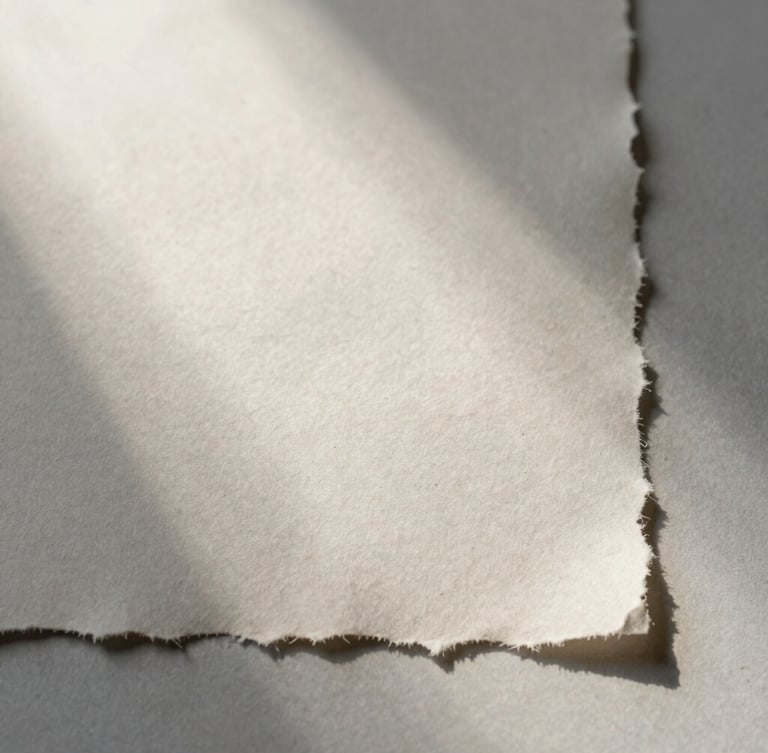 A close-up of textured handmade paper with raw deckled edges, soft morning mist light casting gentle shadows across the surface, minimalist composition.
