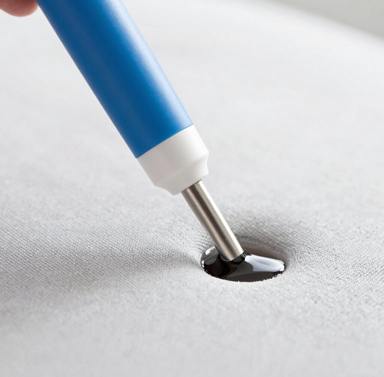 Macro photograph of a professional extraction cleaning nozzle pulling dark water out of a light grey fabric sofa, bright high-key daylight, clean blue and white tones, sharp focus.
