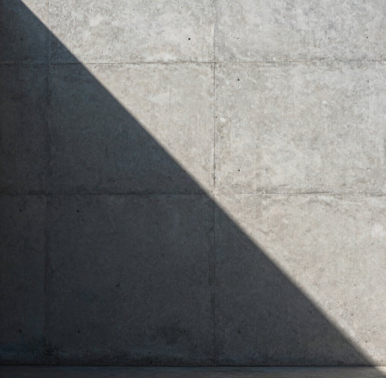 A sharp shaft of morning light cutting across a minimalist concrete wall, casting a crisp geometric shadow, architectural, sober, raw texture.