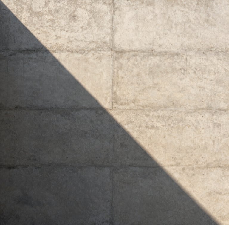 Perfect vertical alignment of a raw concrete wall, a sharp triangular shadow casting across its textured surface, warm natural afternoon light, minimalist composition, 3:4 portrait aspect.