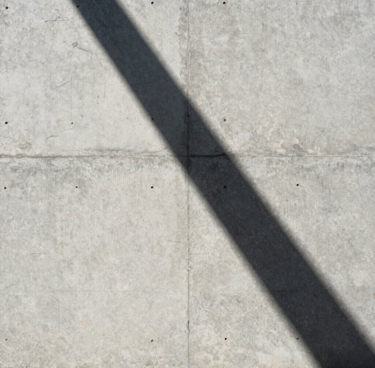 Perfect vertical shot of raw concrete wall meeting a sharp shadow line under harsh tropical sunlight, architectural abstraction, minimalist framing
