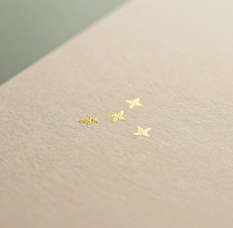 Macro close-up of delicate gold foil details on a textured cream paper, soft golden-hour light, shallow depth of field.