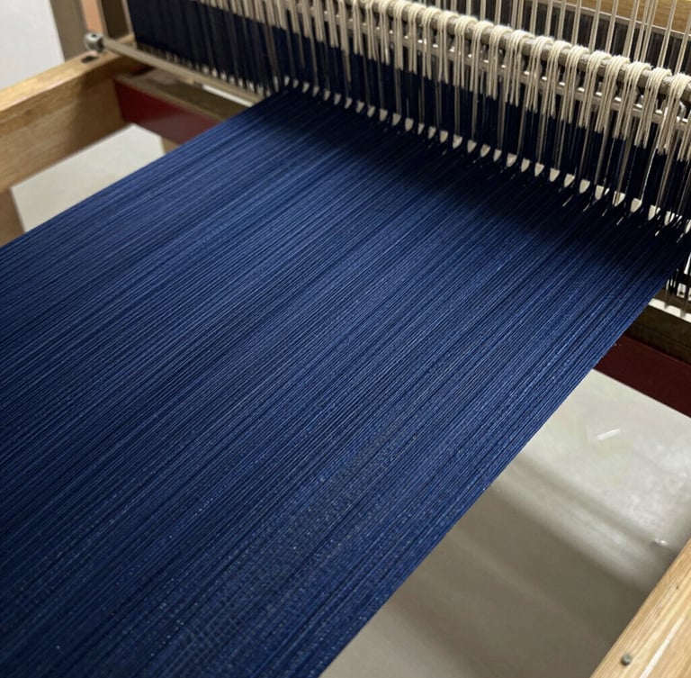 Macro close-up of deep indigo warp threads stretched tightly on a modern industrial loom, natural workshop light highlighting thread density and texture.