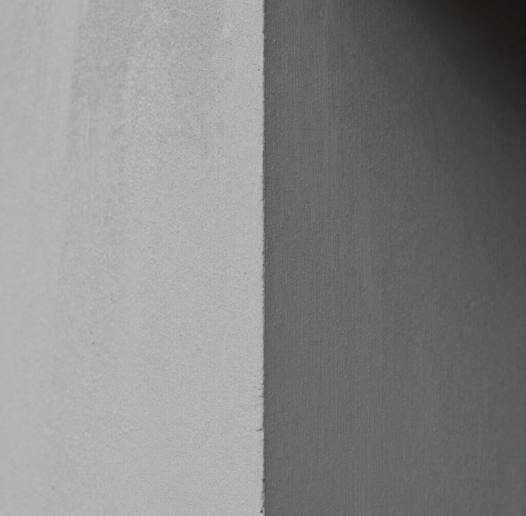 Crisp architectural photography, tight macro shot of raw plaster texture meeting a sharp corner, natural overcast daylight, desaturated slate tones, 35mm lens.