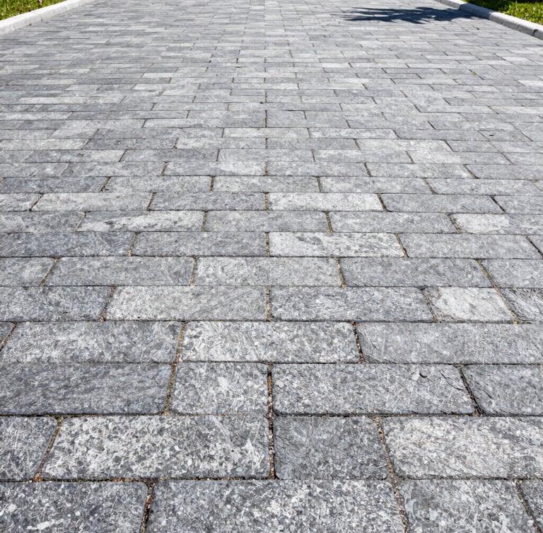 Low-angle architectural shot of a perfectly leveled slate gray paver driveway in Sarasota, bright midday Florida sun, sharp focus on interlocking joints.