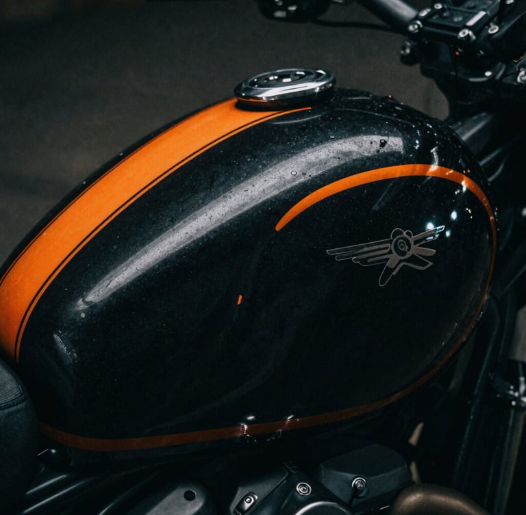 Extreme close-up of a custom-painted motorcycle tank with sharp orange pinstriping, dark dramatic photography, low-key chiaroscuro lighting, deep charcoal tones, 35mm film grain