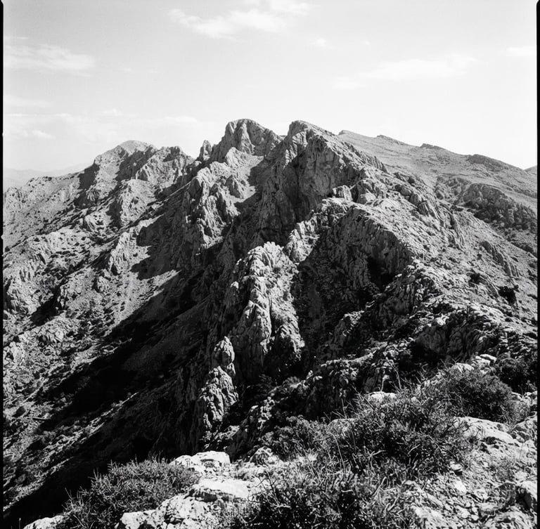 Stark documentary portrait of a rugged limestone mountain ridge in Arcadia, harsh midday sun casting deep black shadows, uncropped 35mm film grain.
