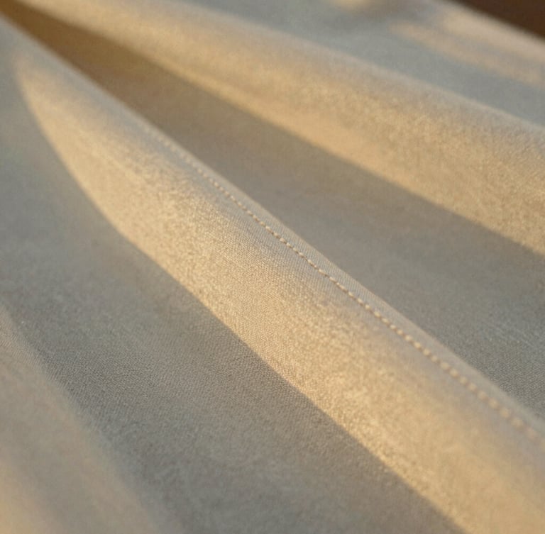 Extreme close-up of a hand-stitched silk hem in warm golden hour light, focusing on the refined texture of heritage-mill fabric, shallow depth of field, 35mm film style.