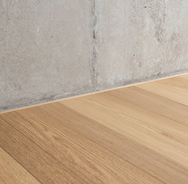 Close-up of pristine custom oak flooring meeting a raw concrete wall with absolute precision, sharp architectural lines