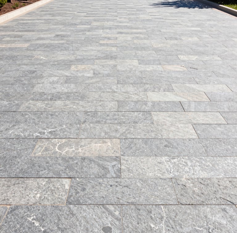 Low-angle wide shot of a newly completed interlocking stone driveway in bright morning sunlight, clean slate gray and limestone tones, sharp architectural lines, high-contrast details.