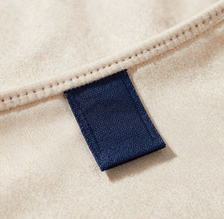 Macro shot of a heavy-weight organic cotton garment collar with a custom-woven fabric label stitched precisely, natural daylight, soft shadows
