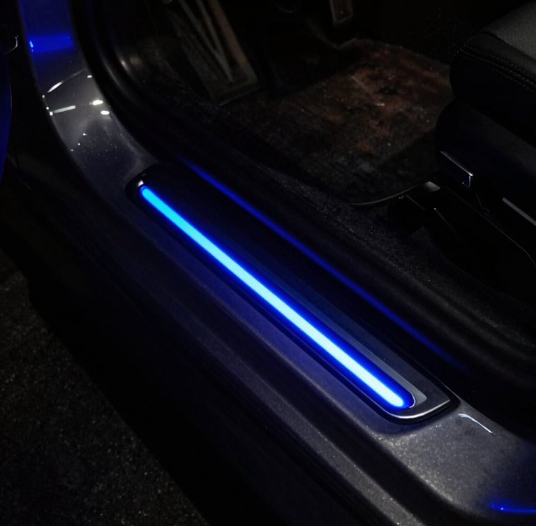 Moody night photography of a sports car door sill glowing with vibrant electric indigo LED light, reflecting off dark metallic door frame.