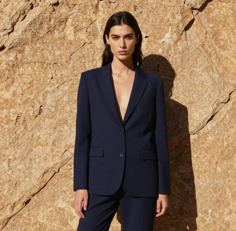 High-contrast outdoor portrait of a model standing against a sheer sandstone cliff, harsh direct midday sunlight, sharp shadows, 35mm editorial photography