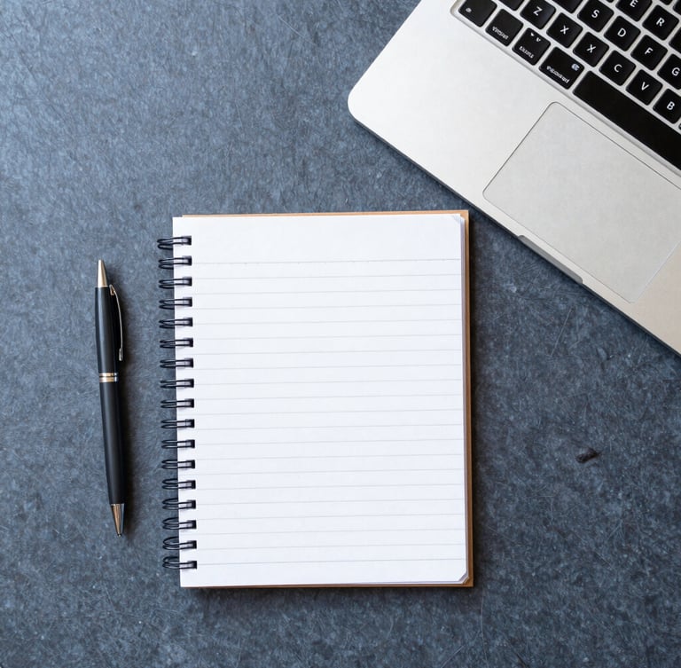 Overhead flat-lay of an organized desk with a notebook, pen, and laptop, bright natural daylight, sharp focus, 35mm