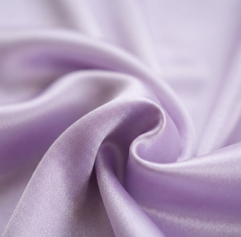 Macro close-up of high-sheen lavender satin fabric draped elegantly with soft natural daylight casting gentle shadows, bright editorial photography, shallow depth of field