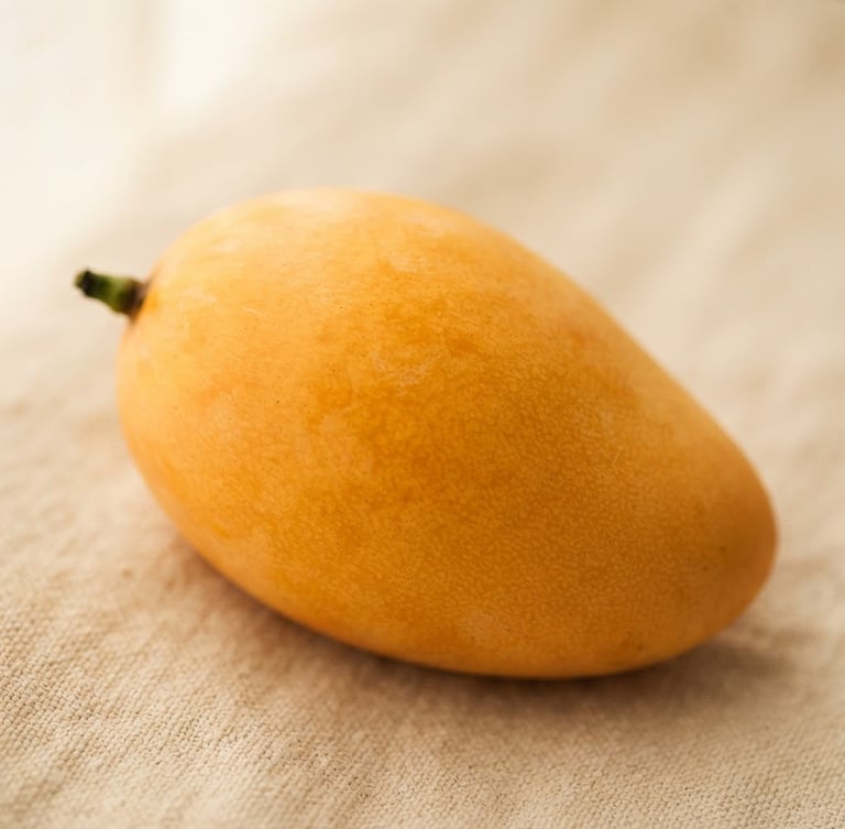 Macro close-up of a pristine, unblemished golden mango on a cream linen background, soft diffused window light, rich warm tones, shallow depth of field.