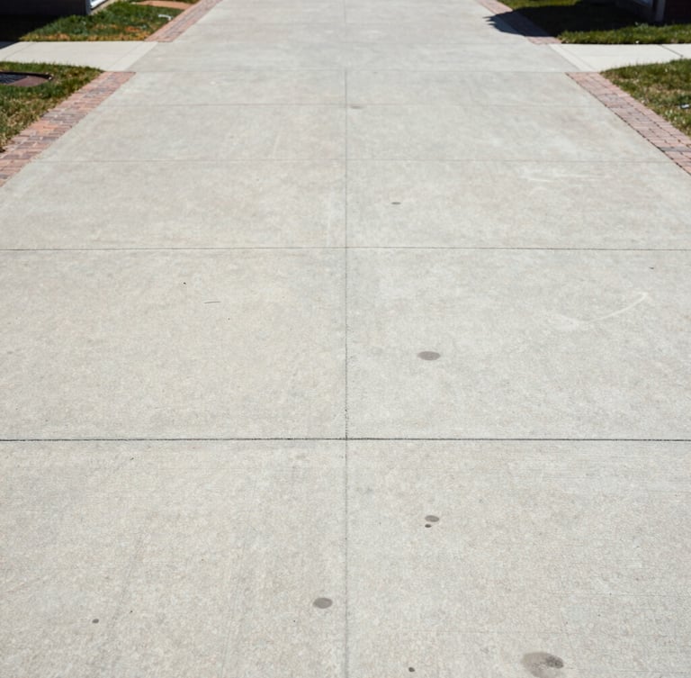 Straight-on architectural shot of a pristine concrete driveway and brick walkway, clean and free of stains, bright Wisconsin sun.