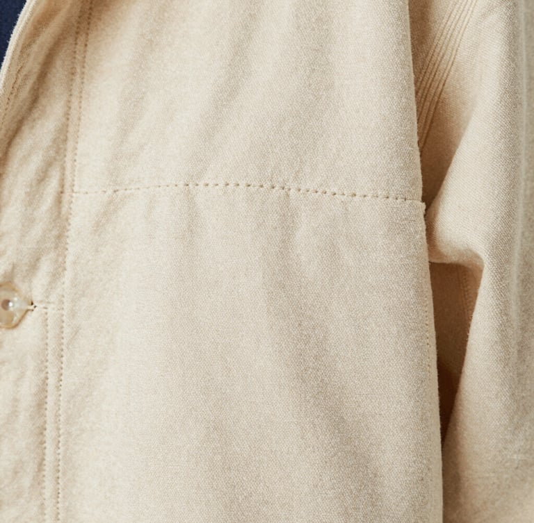 Tight macro shot of double-stitched seams on a heavy cream canvas jacket, showing tactile fabric weave, soft natural light