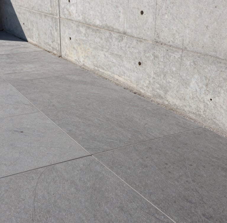 Close-up of premium stone flooring installation next to a raw concrete wall, clean architectural lines, sharp daylight.