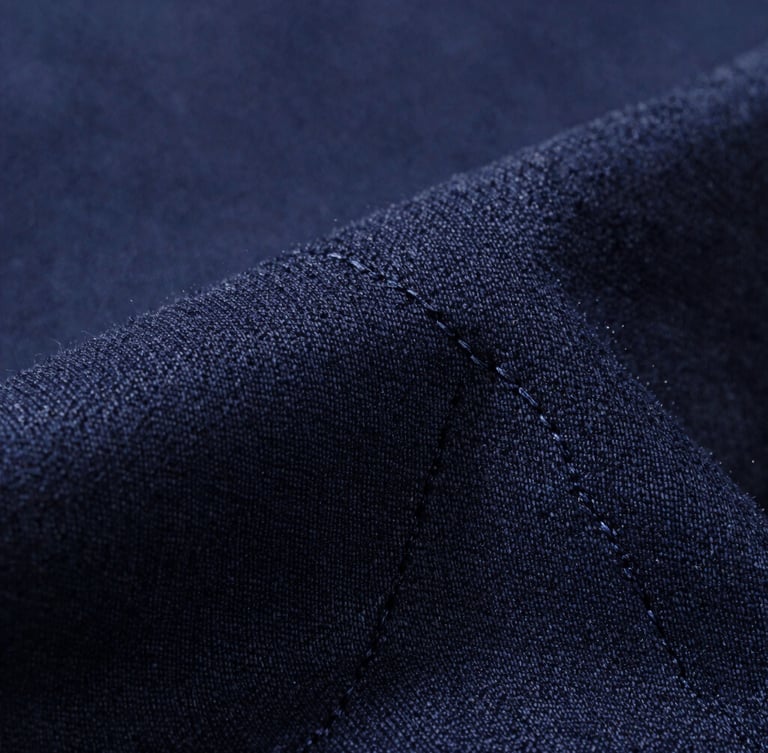Macro close-up of premium dark navy cotton weave, bright directional light highlighting the fine textile fibers and flawless double-stitch line, minimalist composition.