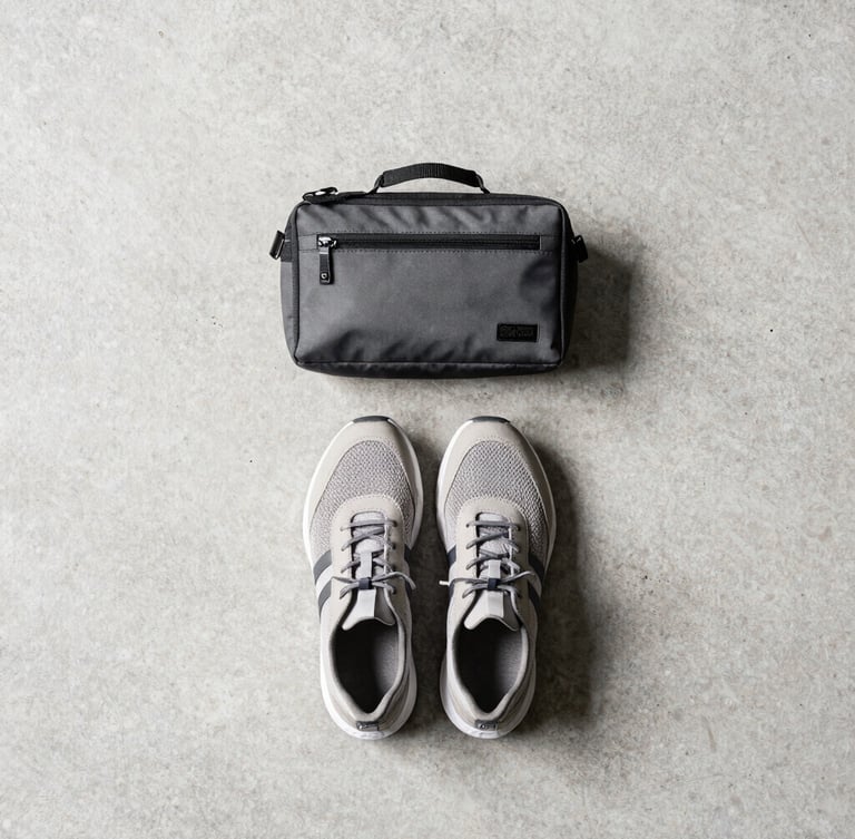 Overhead knolling flat-lay of technical travel accessories, a pair of lightweight shoes, and a compact tech pouch on a concrete background