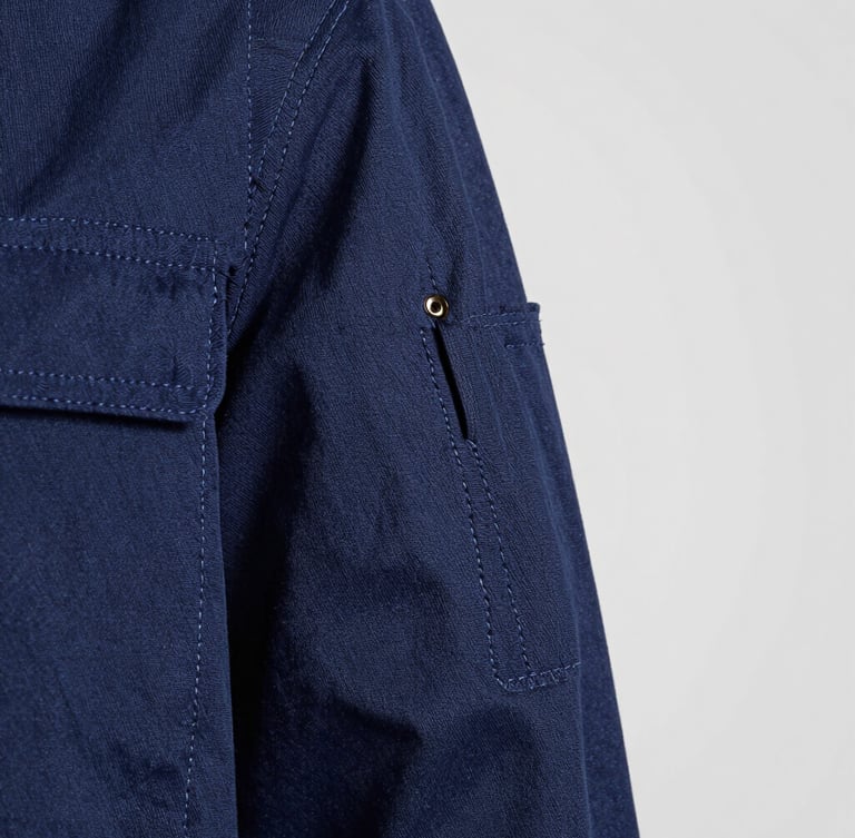 Extreme close-up of heavy-duty double stitching on a navy blue industrial work jacket, bright studio lighting highlighting the thread texture and stitch density, clean slate gray background.