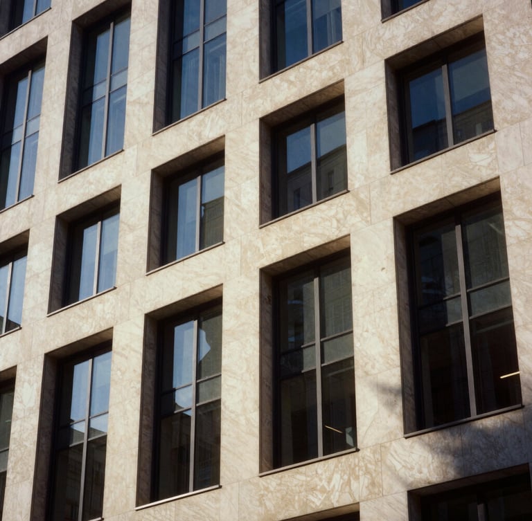 Architectural close-up of a modern limestone office building facade, sharp diagonal shadows, warm sunlight, editorial corporate photography
