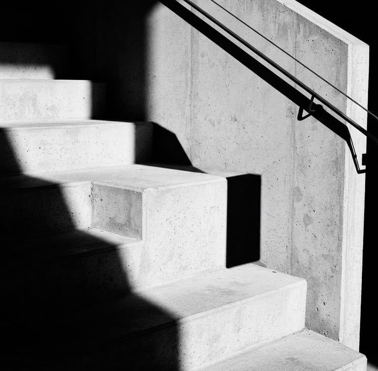 Stark minimalist architectural crop of concrete corporate office stairs, sharp geometric shadows, direct harsh sunlight, high-contrast monochrome, 35mm lens