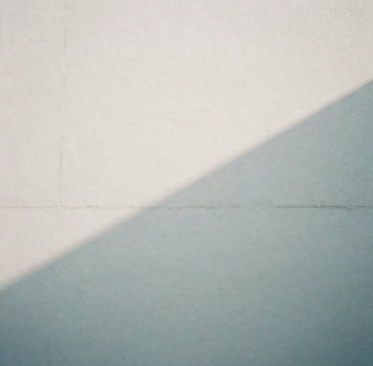 Abstract architectural shadow falling across a pale concrete wall, soft overcast daylight, desaturated cool tones, high grain, 35mm lens, quiet atmosphere