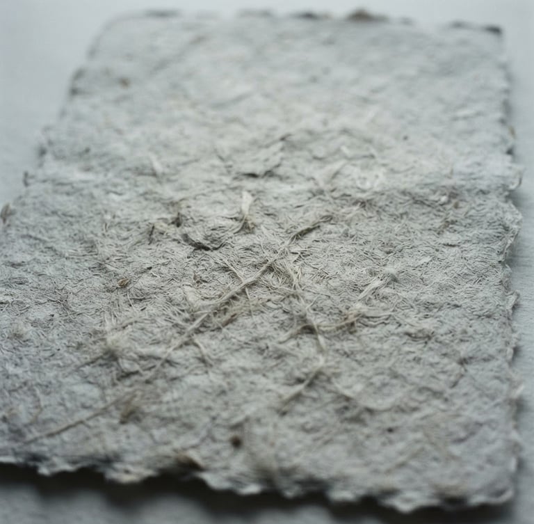 Intimate close-up of textured handmade paper with soft natural shadows, minimalist film photography, desaturated cool tones, high grain, 35mm lens, quiet atmosphere