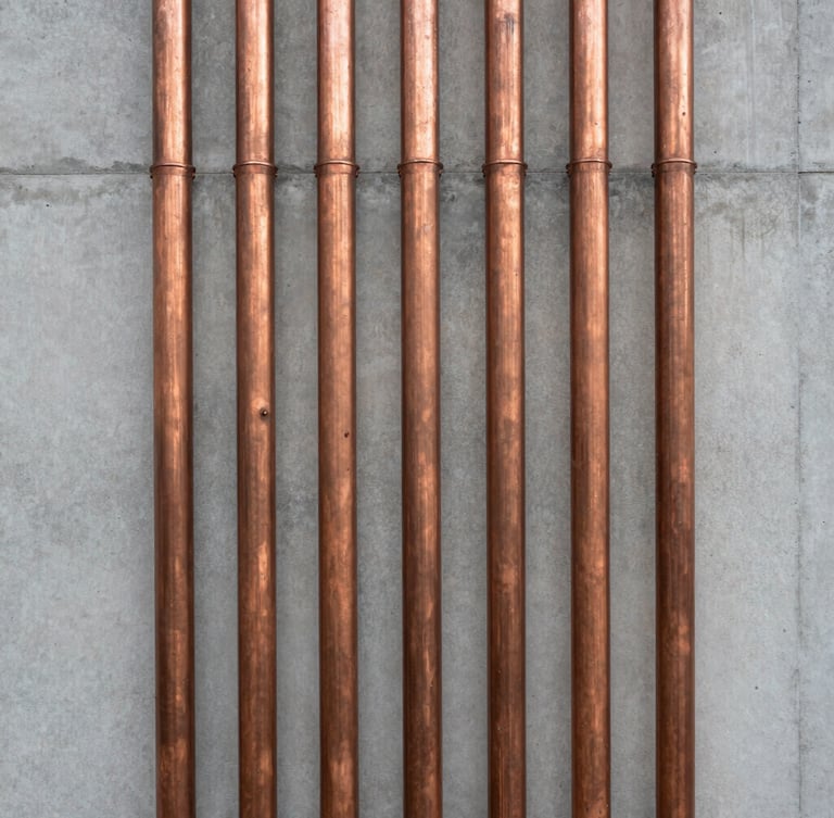 Straight-on architectural shot of perfectly aligned copper conduits running vertically down a minimalist concrete wall, natural side lighting, symmetrical composition.